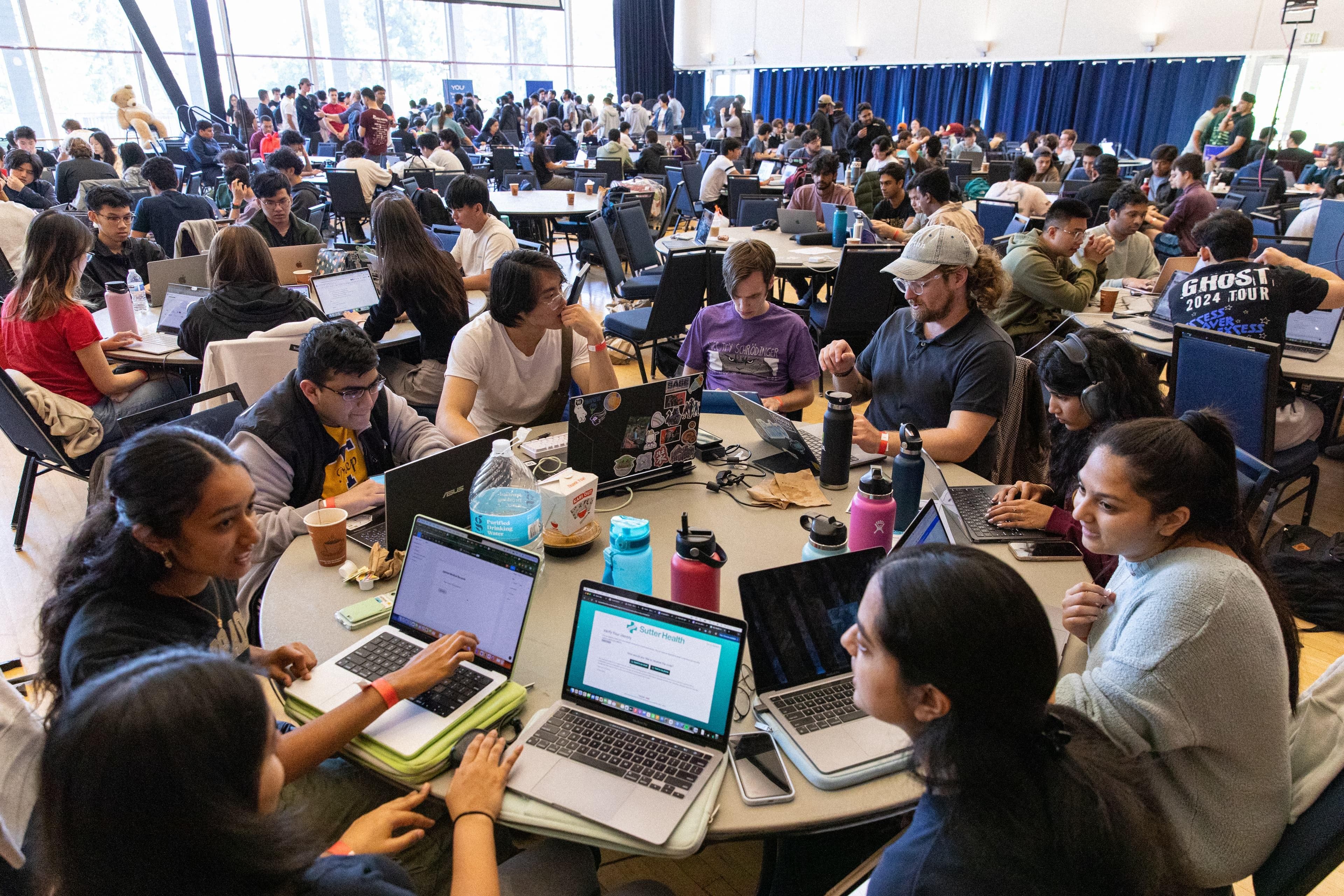 A packed hall of students building at the hackathon